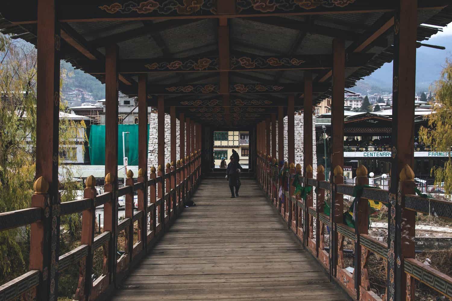 person in black jacket walking on wooden bridge