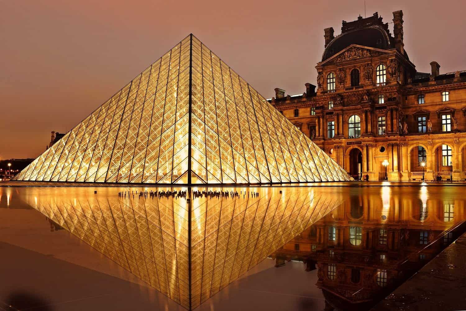 the lovre museum clear glass pyramid museum contrasting with historical stone building during golden hour. architecture like this makes paris one of the best travel destinations for design lovers