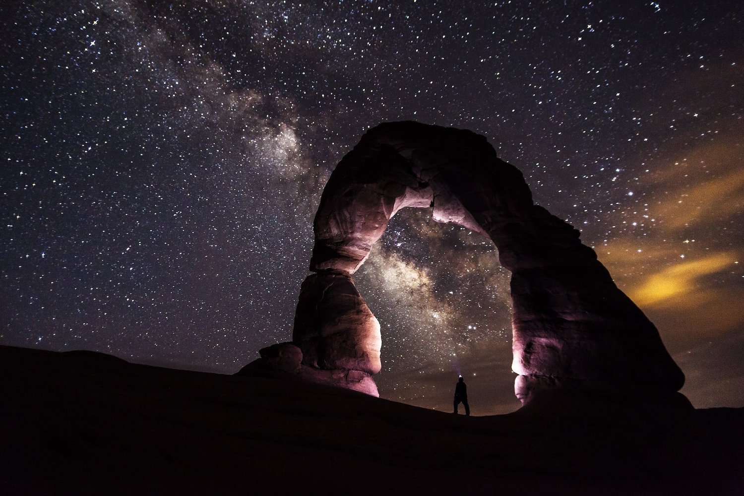 person standing under a rock formation on a starry night. pondering the vastness of the universe / god