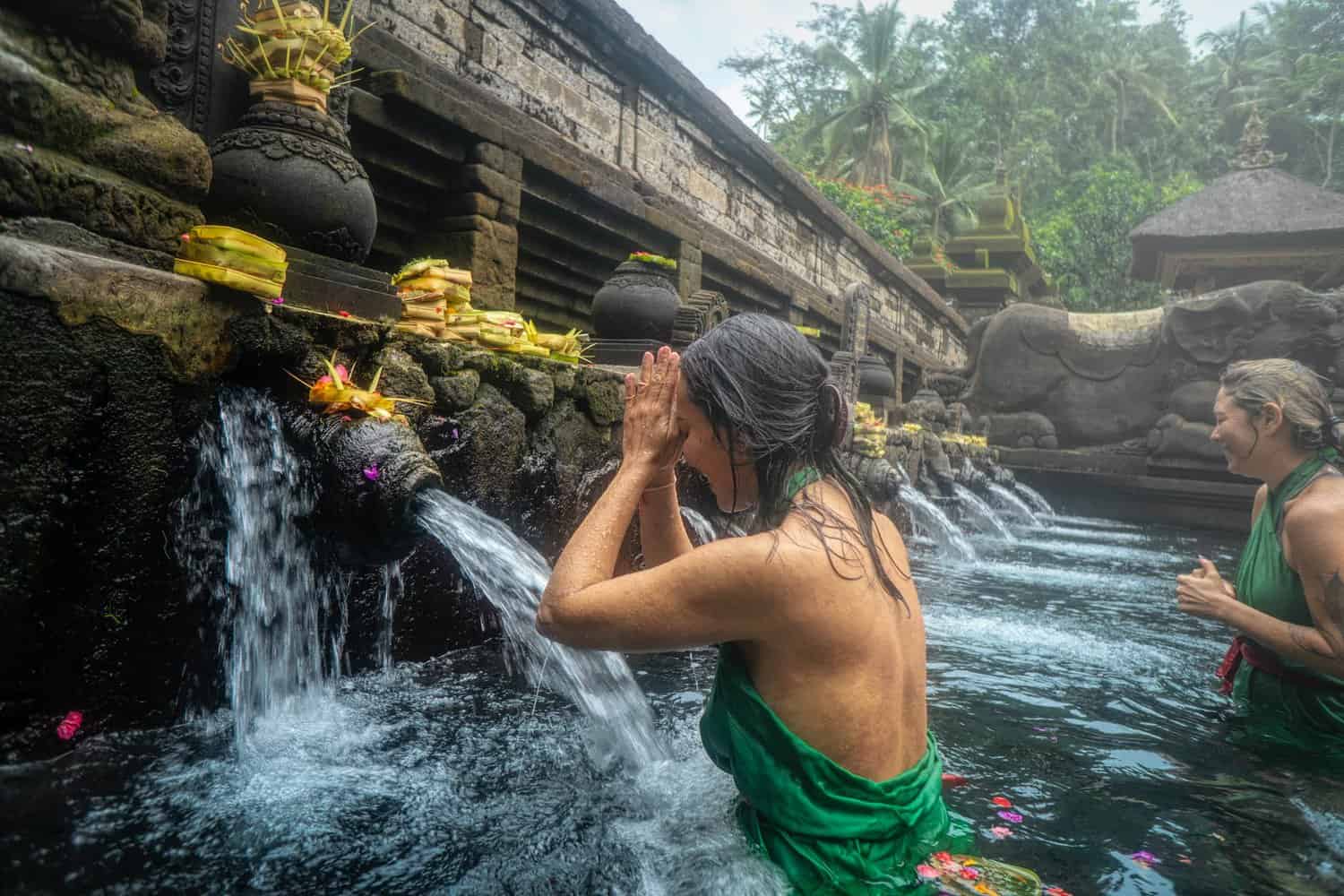 woman standing in front of flowing water temple in bali which holds alot of sacred meaning.
