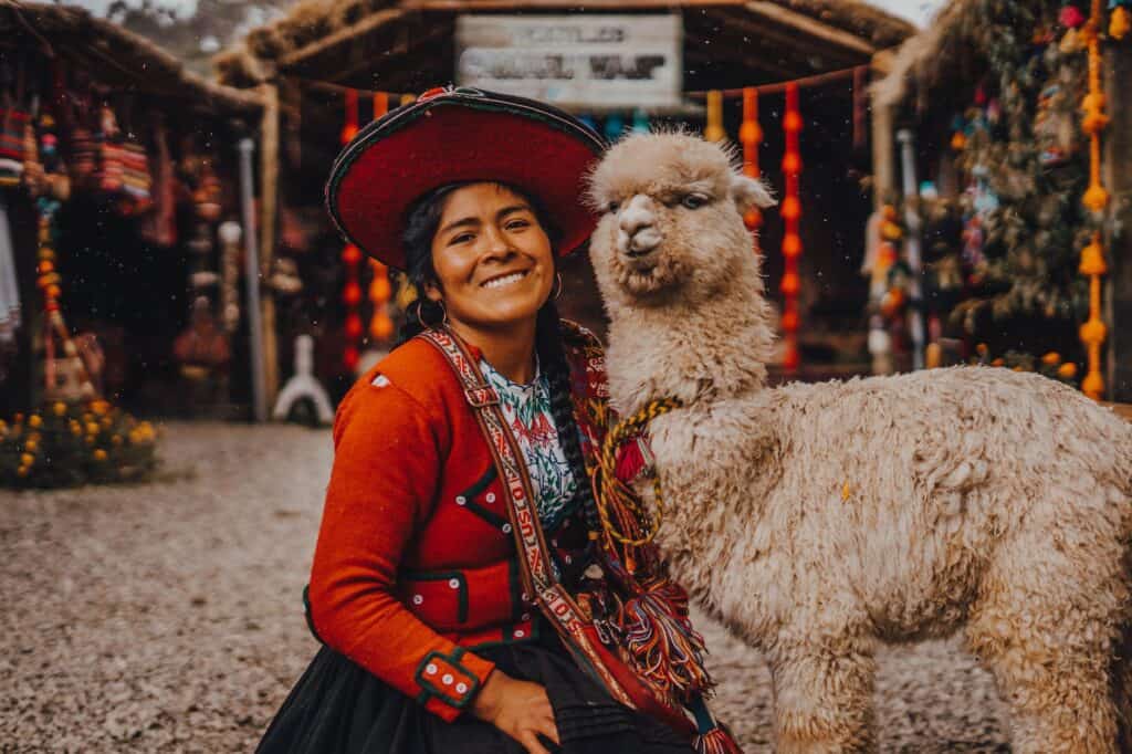 young woman in traditional clothing and sitting next to an alpaca impact of tourism on culture