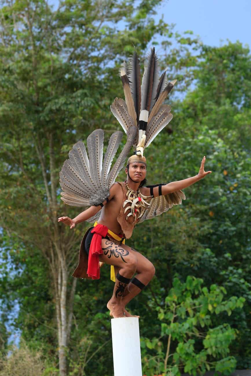 man dressed in traditional aztec costume with feathers standing on concrete pole