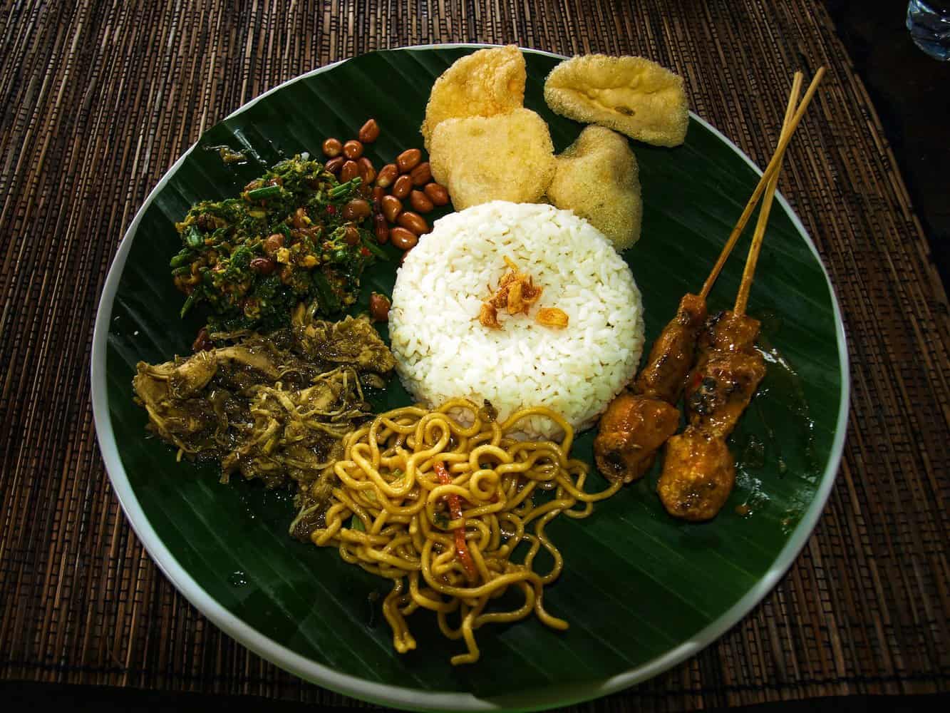 nasi campur: a famous balinese dish/ selected form a buffet. a green plate topped with lots of food. bali vs thailand