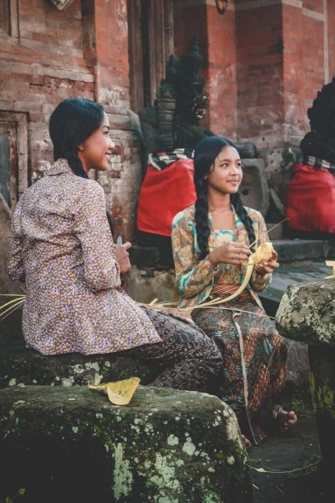 woman holding woven coconut leaf beside woman sitting while holding knife how to experience authentic local culture in indonesia